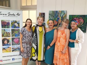 A group of ladies at an art exhibiton with art and an Emma Jacobs Art Banner in the background